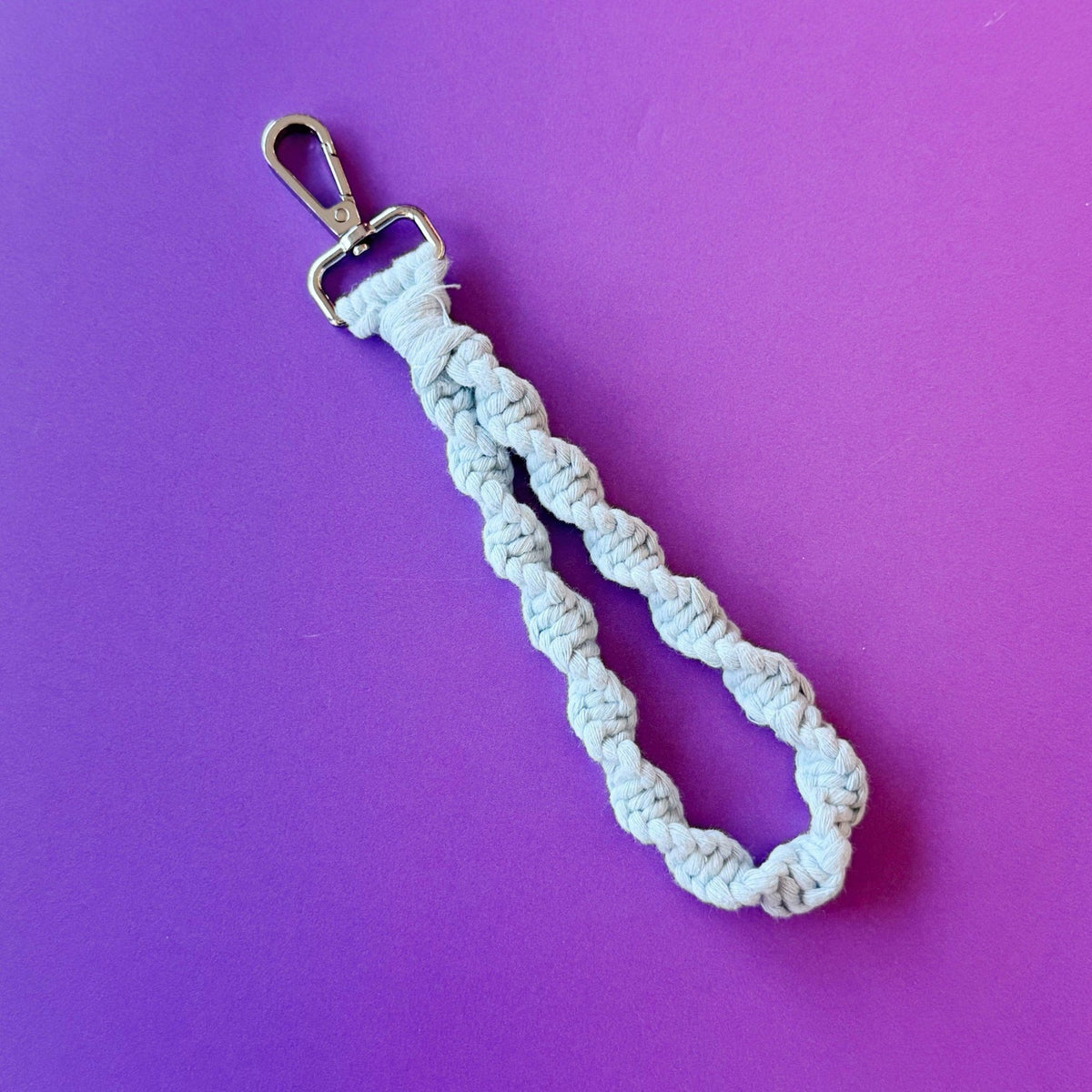 Light blue braided macramé keychain with silver lobster clasp on purple background
